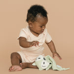 Baby wearing rosy peach organic cotton short sleeve bodysuit and fold-over shorts, holding a green fox toy