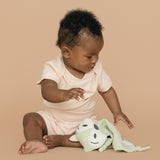 Baby wearing rosy peach organic cotton short sleeve bodysuit and fold-over shorts, holding a green fox toy