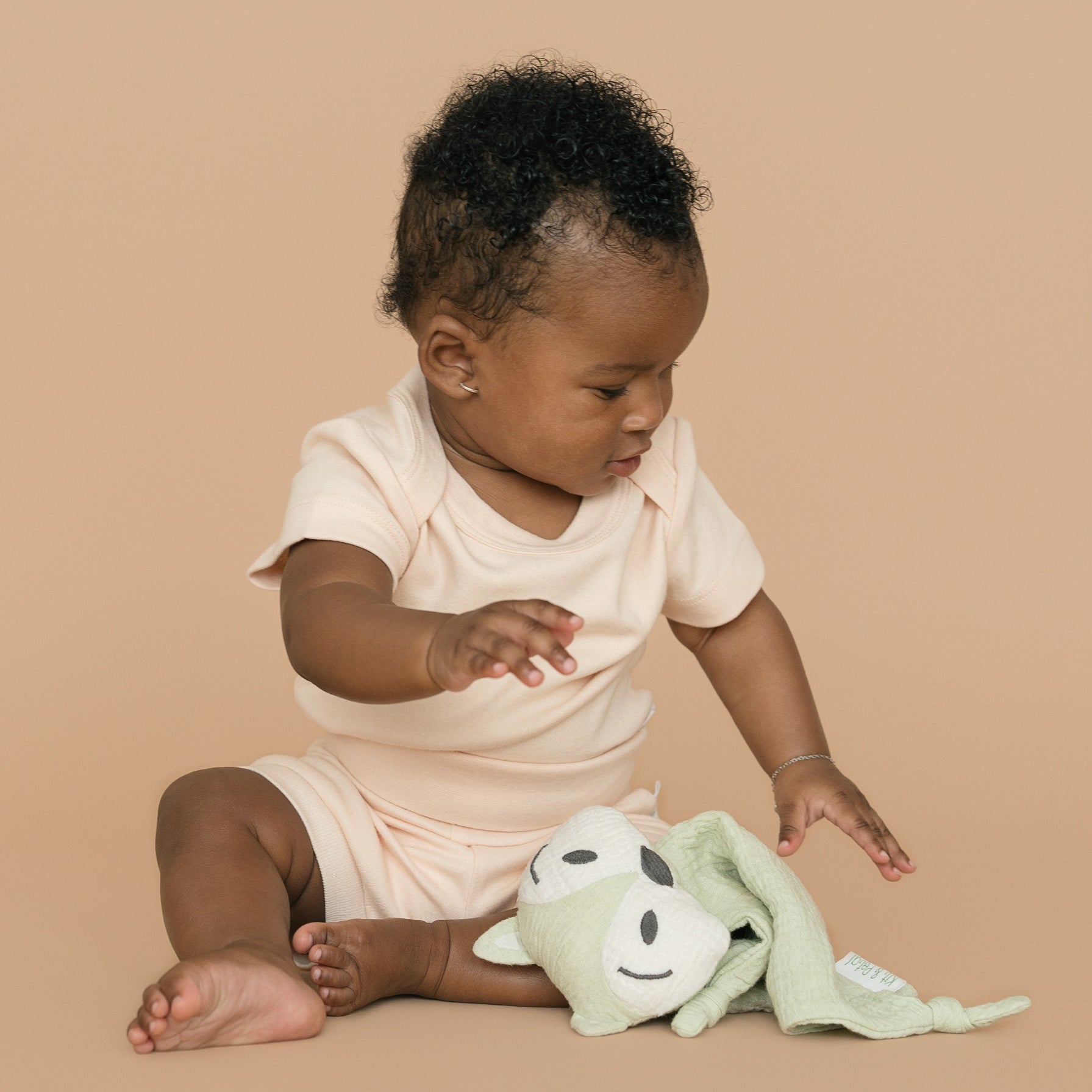 Baby wearing rosy peach organic cotton short sleeve bodysuit and fold-over shorts, holding a green fox toy