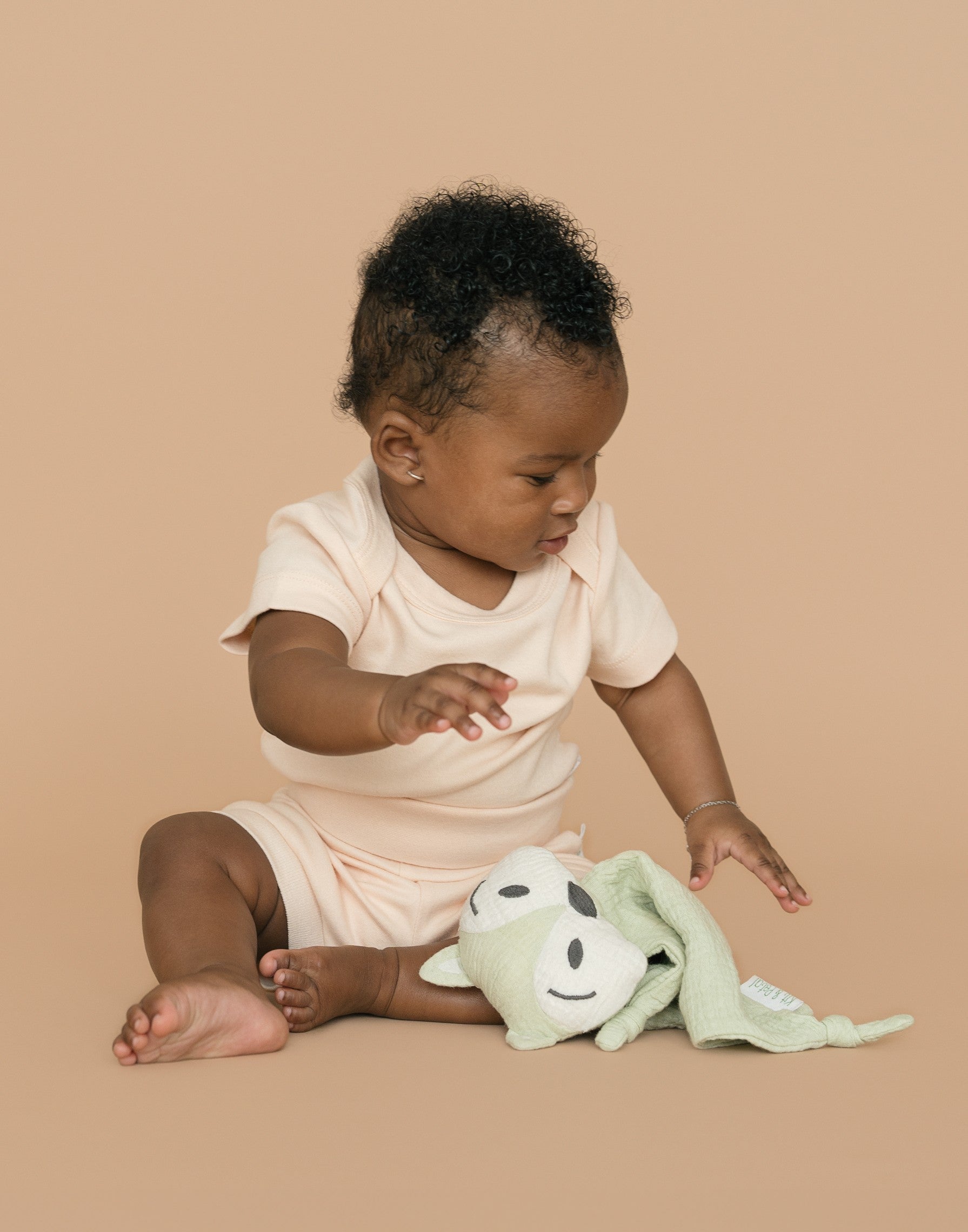 Baby wearing rosy peach organic cotton short sleeve bodysuit and fold-over shorts, holding a green fox toy
