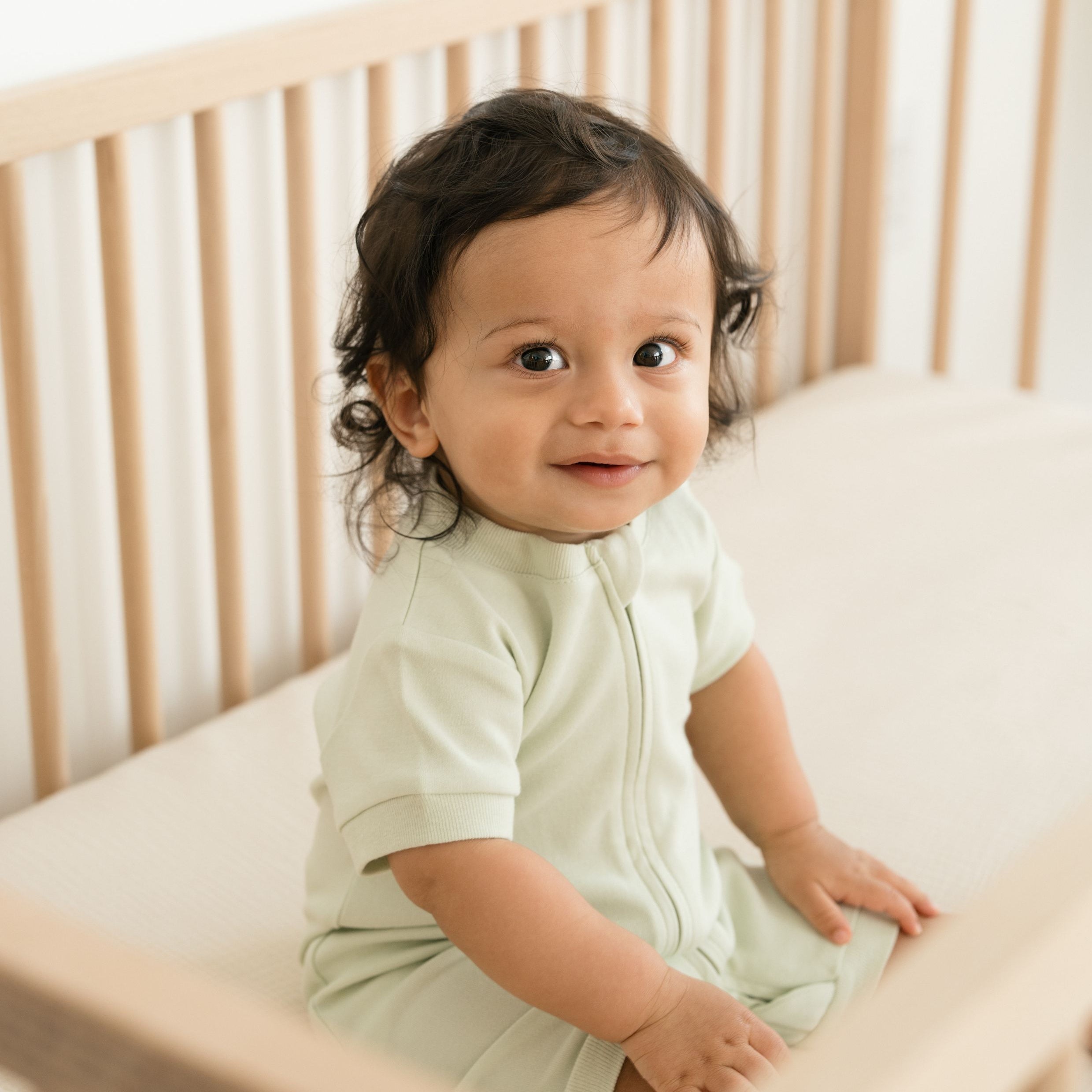 Smiling baby sitting in crib wearing leafy green organic cotton short sleeve romper