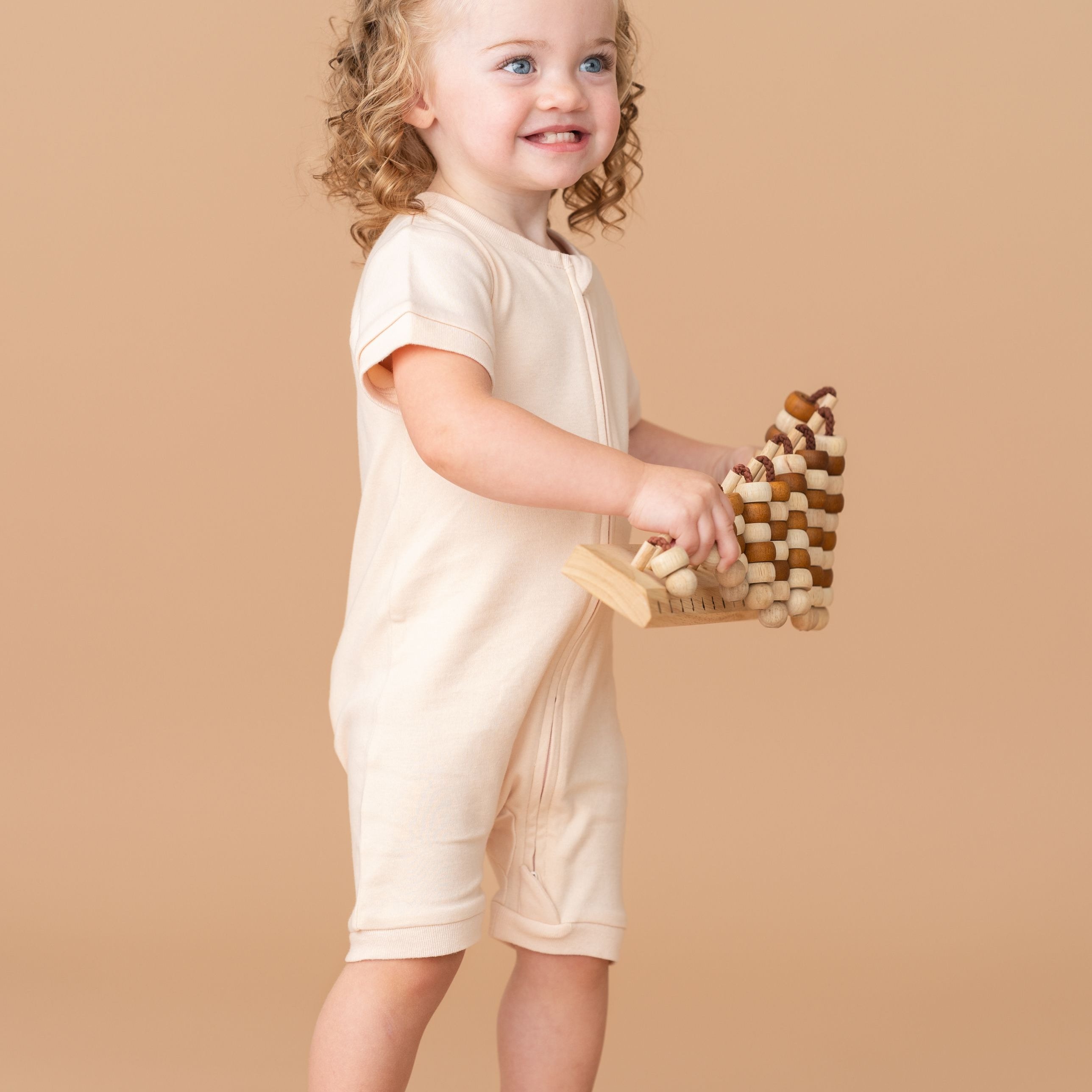 Toddler girl wearing a Rosy Peach organic cotton short sleeve romper, holding a toy.