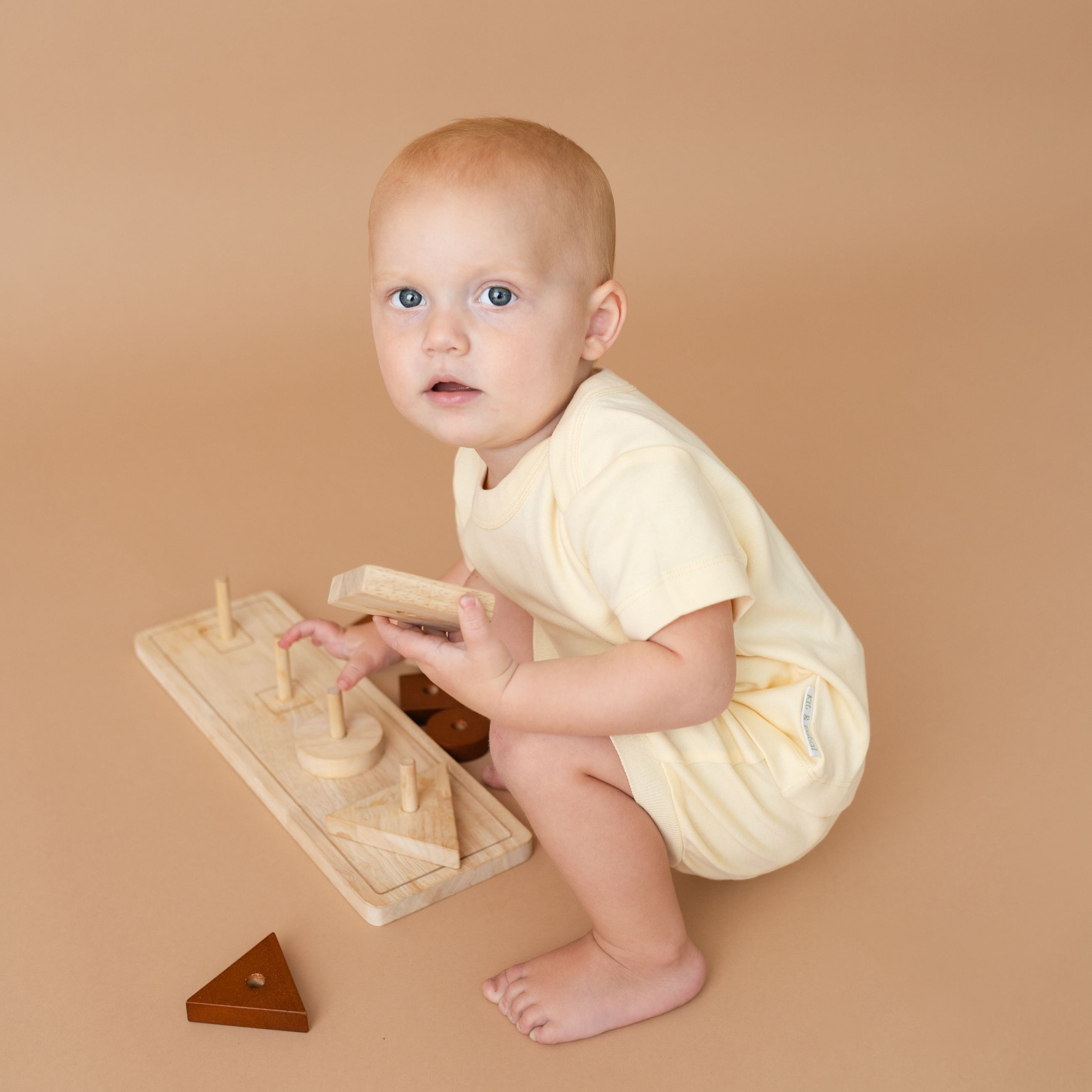 Toddler wearing a Sunny Yellow organic cotton short sleeve shirt and fold-over shorts, playing with a toy.