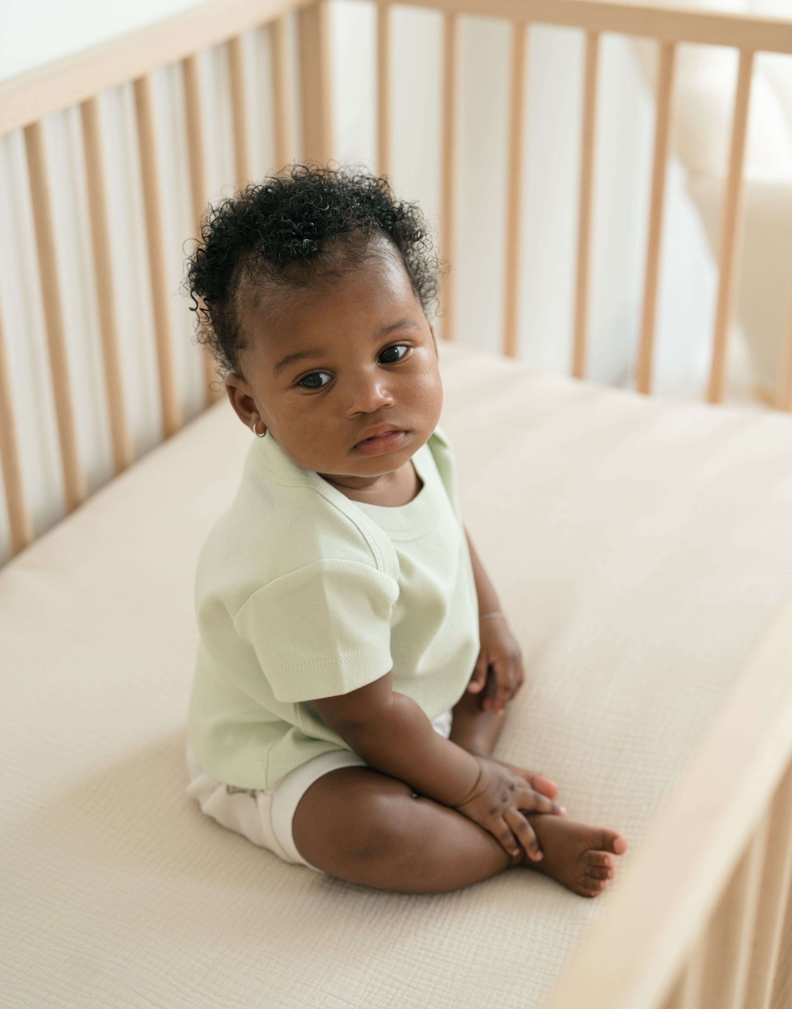 Baby sitting in a crib wearing a Leafy Green organic cotton short sleeve shirt and Forest Friends print fold-over shorts.