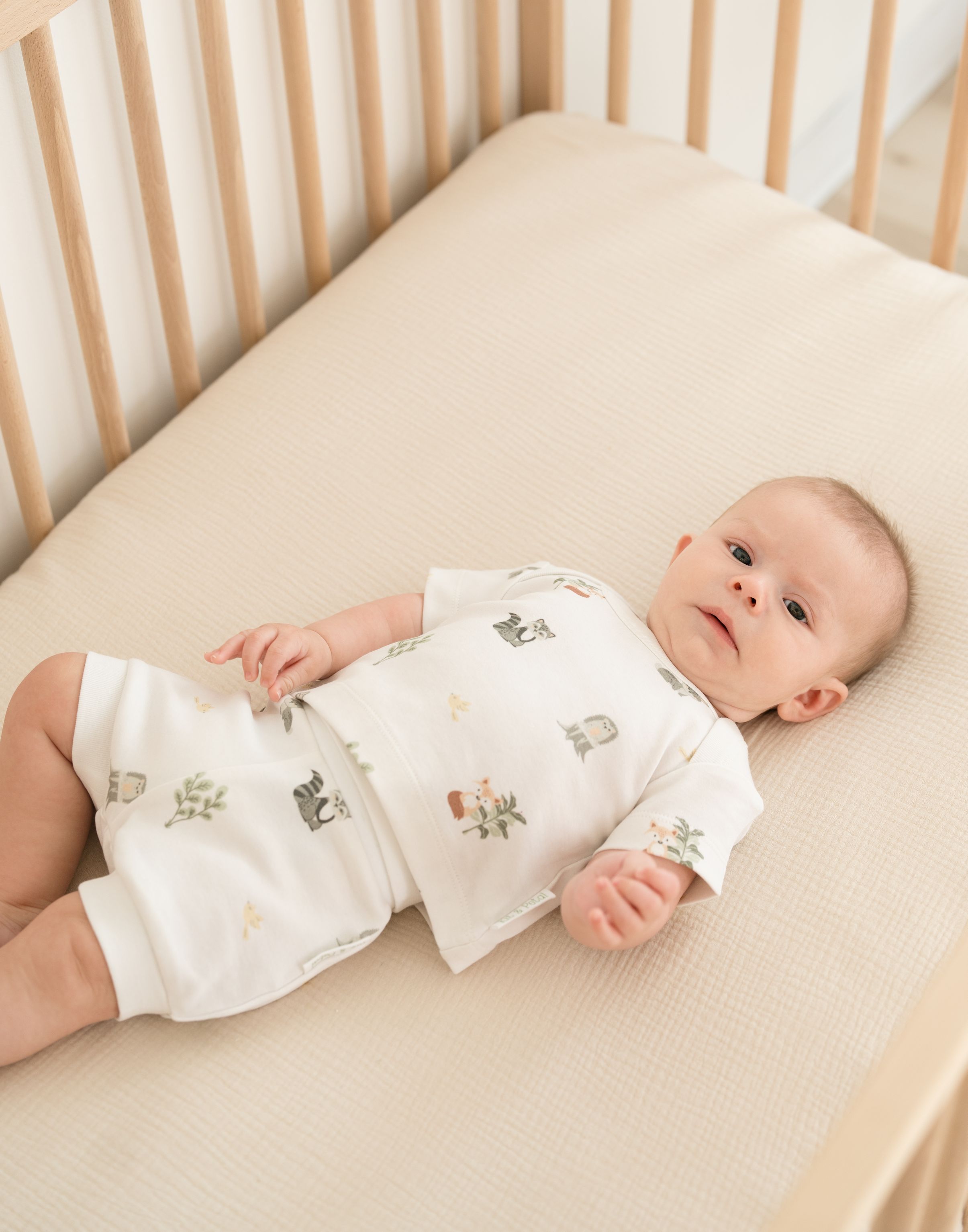 Baby laying in a crib wearing a Forest Friends organic cotton short sleeve shirt with woodland animal print.