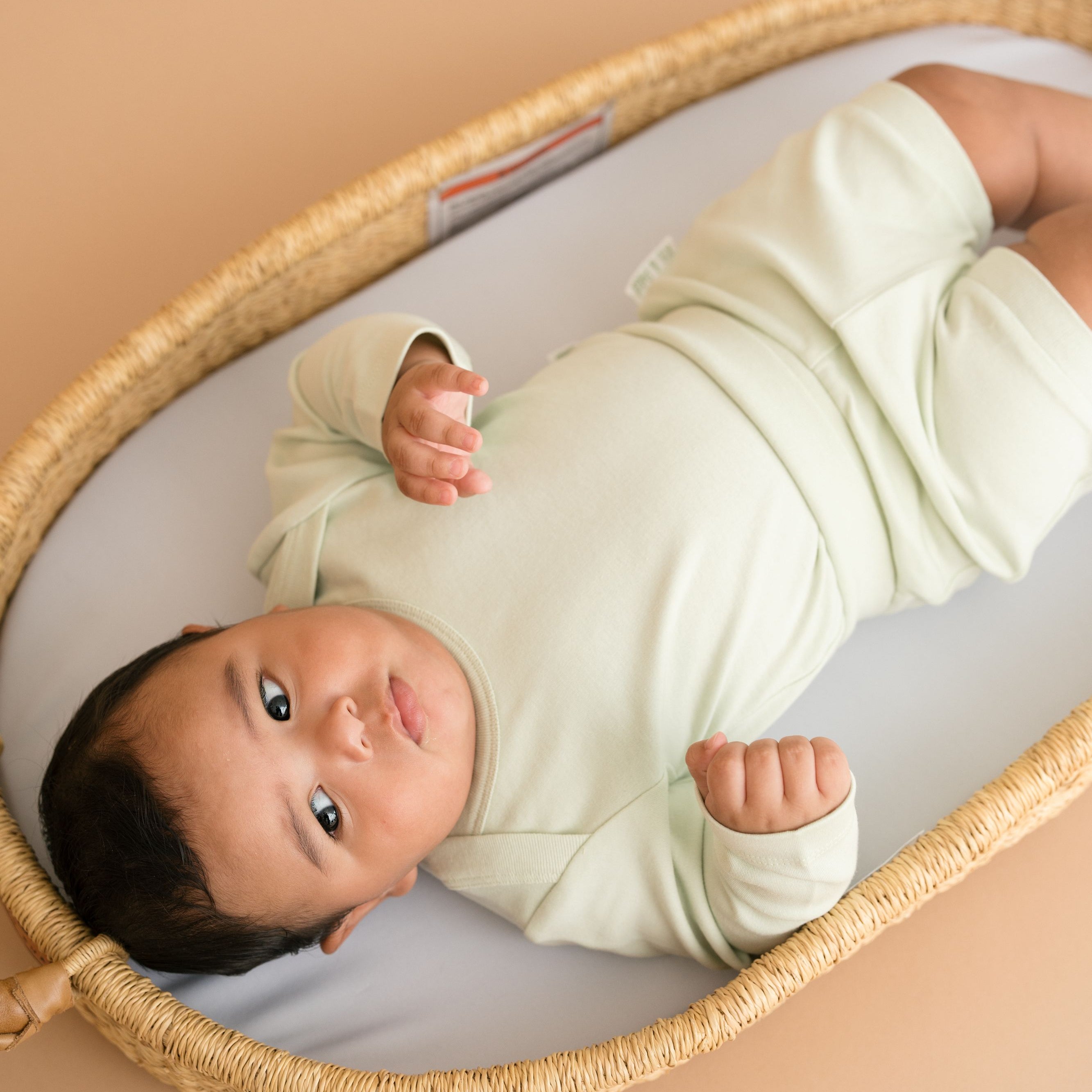 Baby lying in bassinet wearing leafy green organic cotton long sleeve bodysuit and fold-over shorts