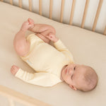 Baby wearing a Sunny Yellow organic cotton long sleeve bodysuit, laying in a crib.