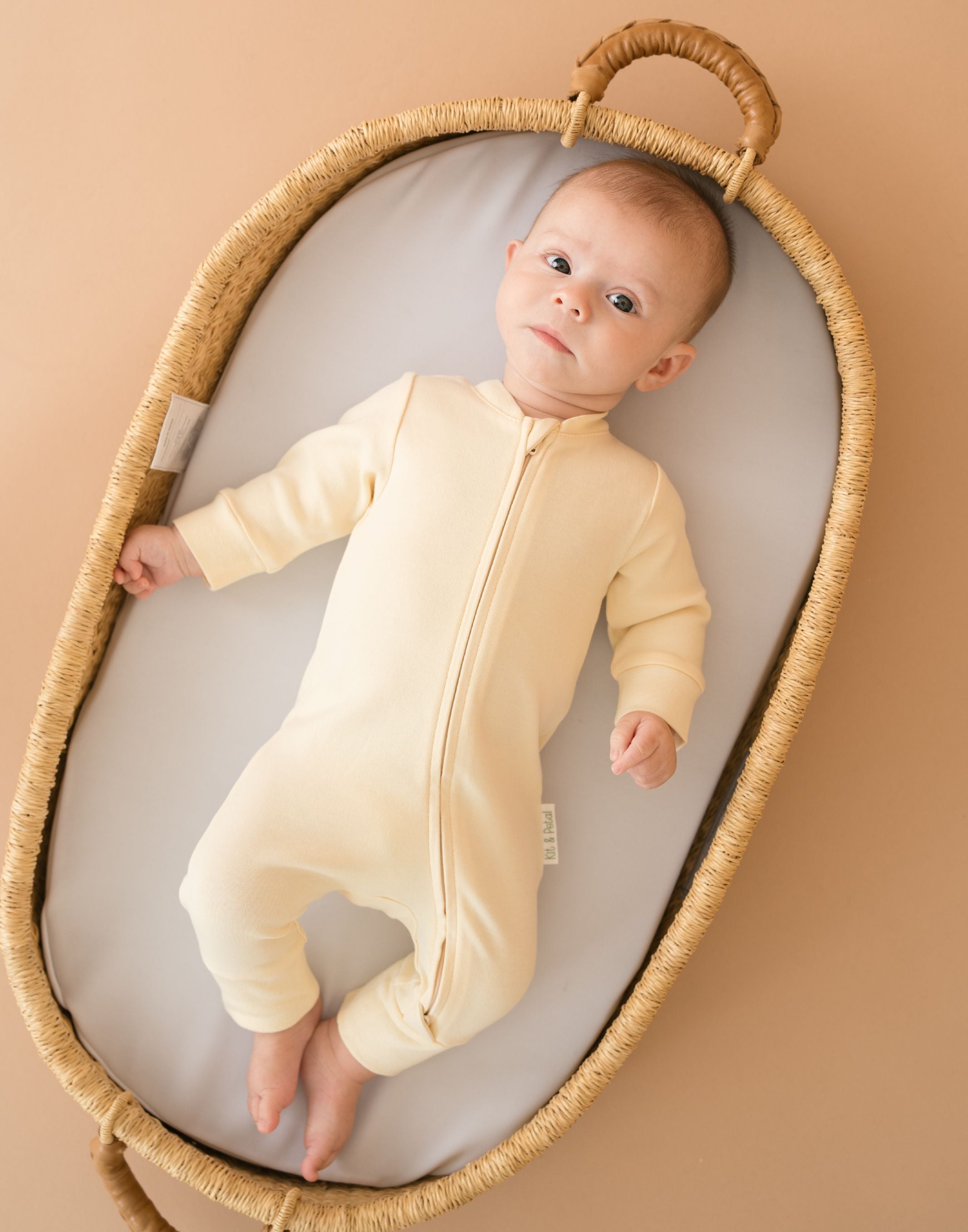 Baby wearing a Sunny Yellow organic cotton long sleeve romper, laying in a bassinet.