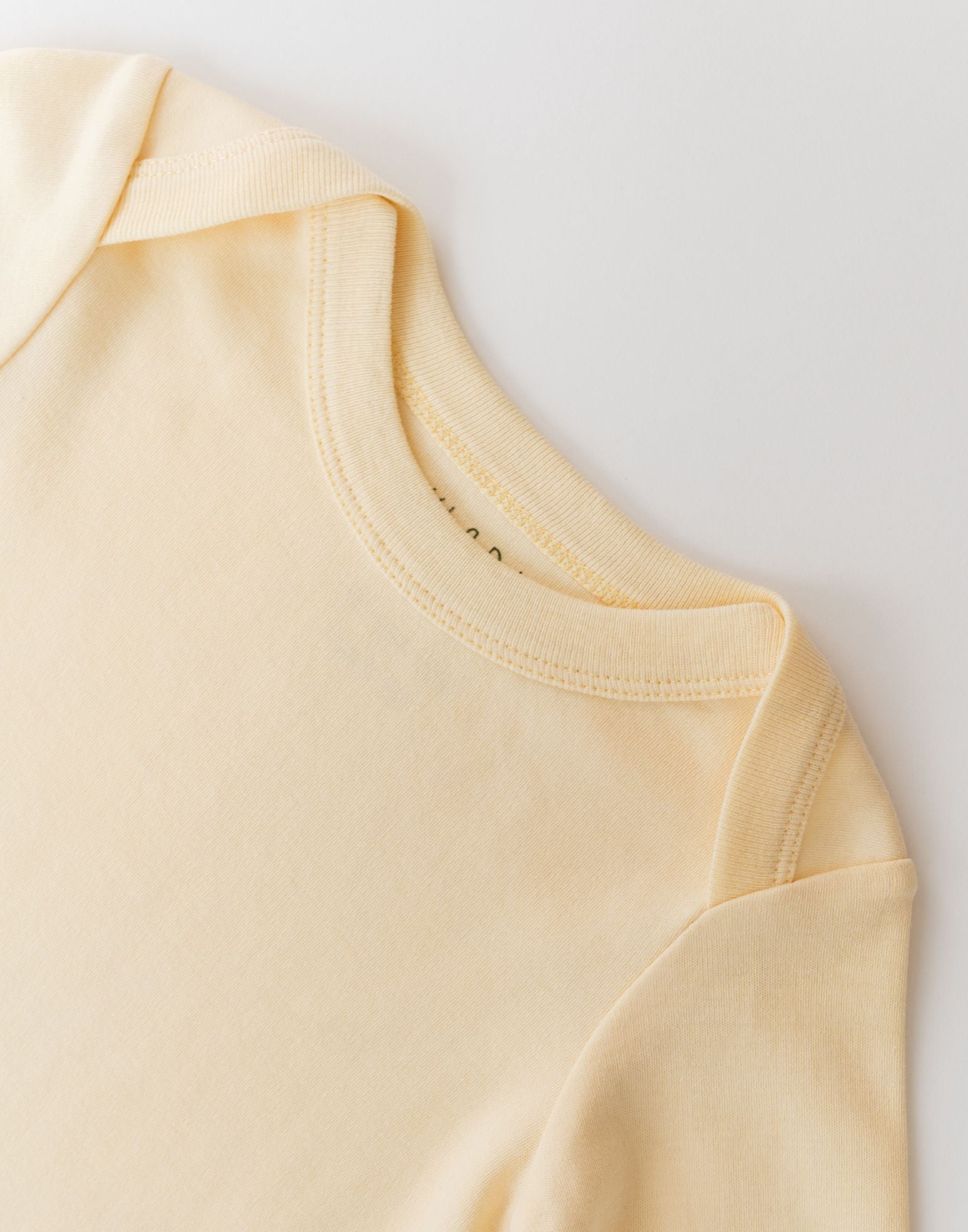Close-up of envelope neckline on sunny yellow organic cotton baby long sleeve shirt