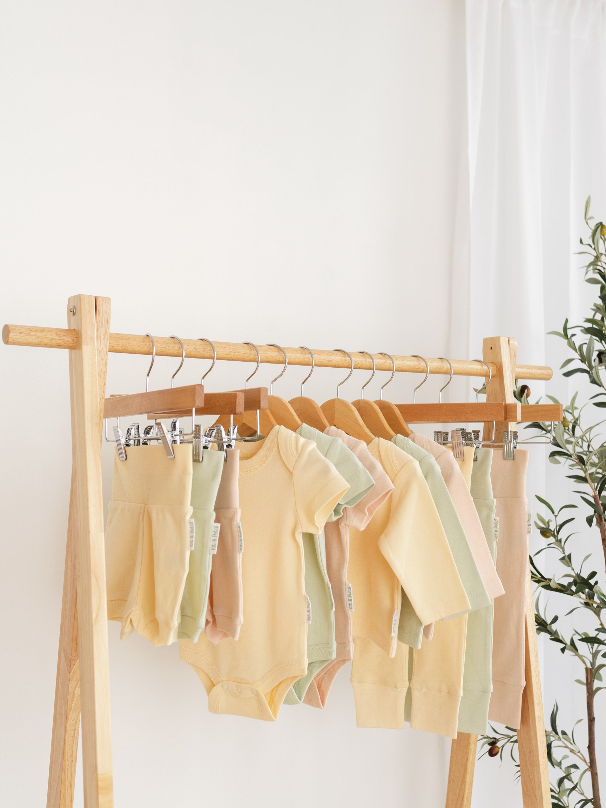 Kit & Petal shorts, bodysuits and pants hanging up on a rack with a plant in the background