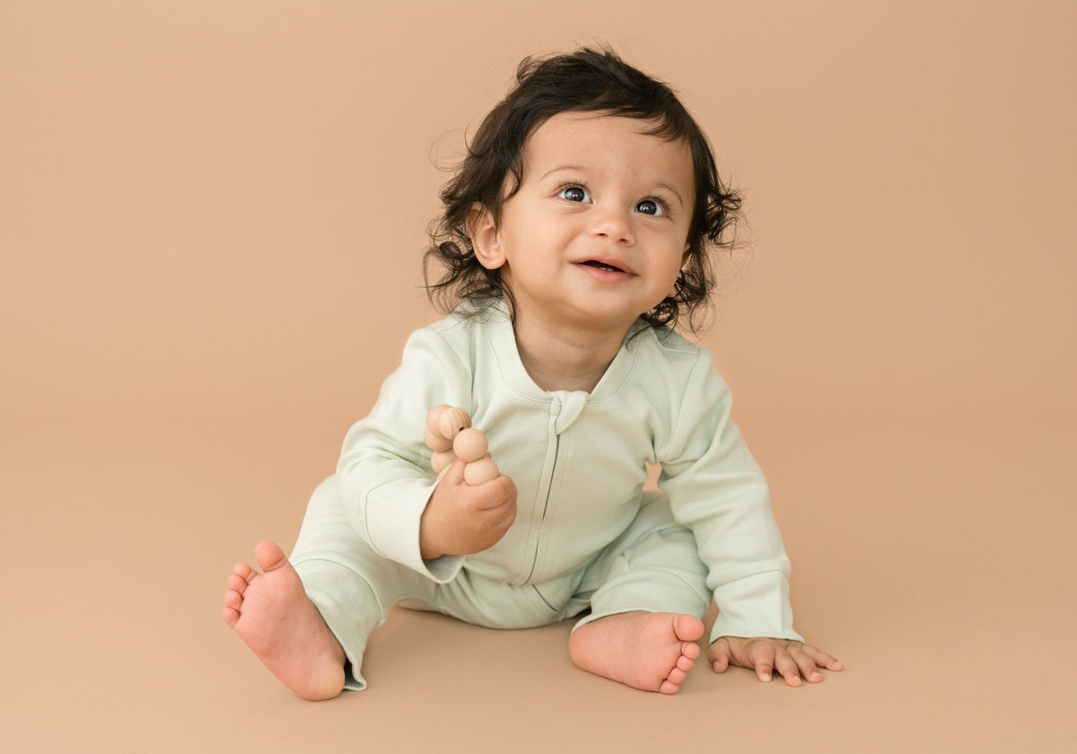 Baby wearing leafy green long sleeve Kit & Petal romper while smiling