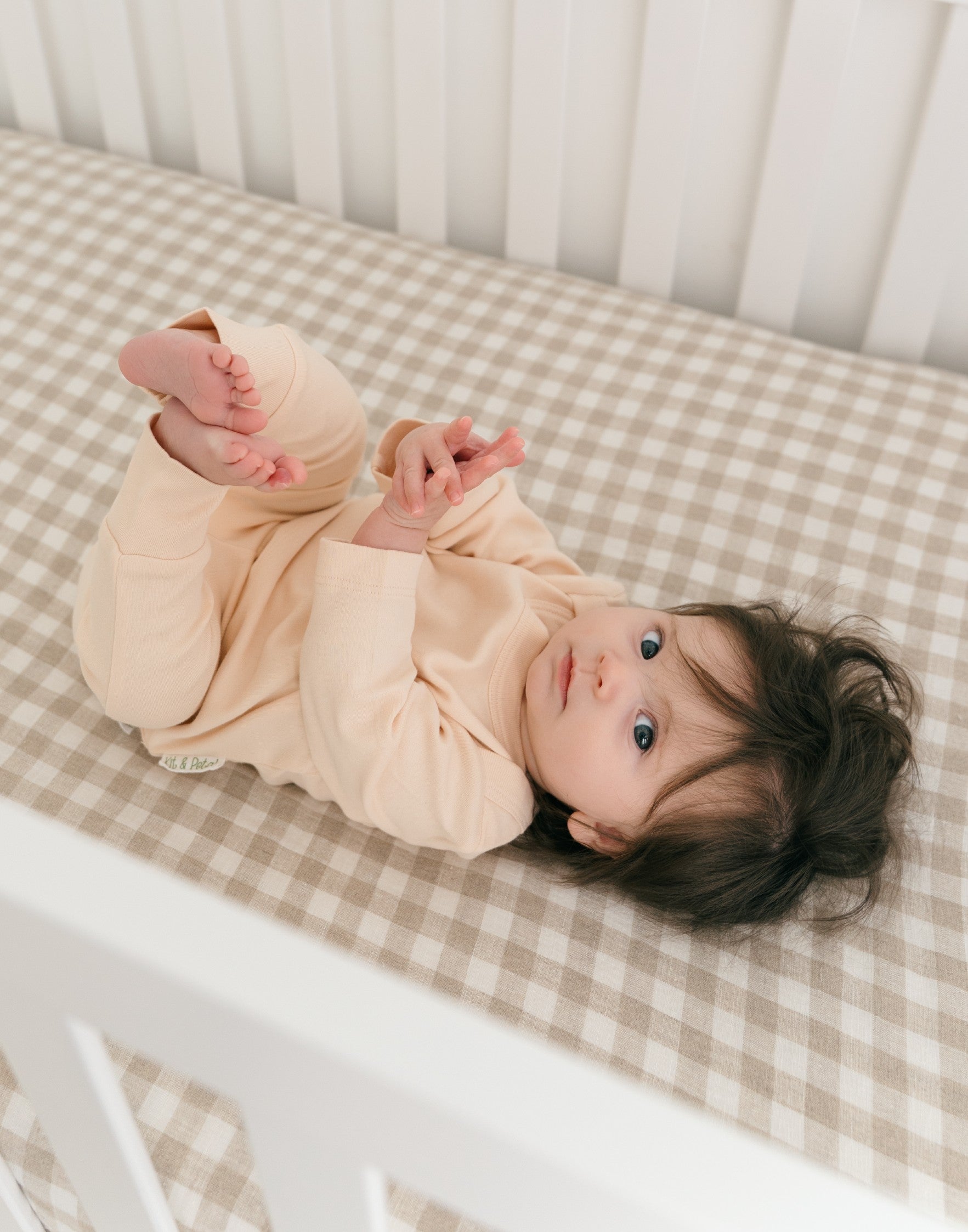 Baby lying in crib wearing rosy peach organic cotton long sleeve shirt and fold-over pants