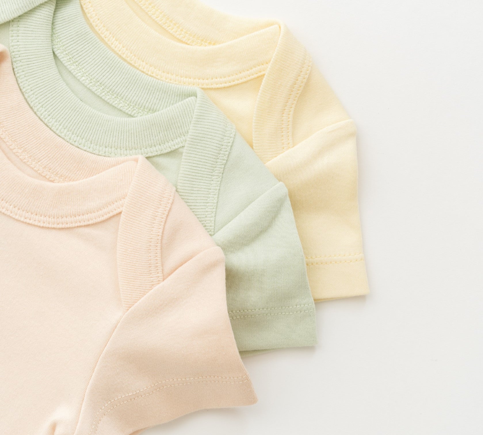 Kit & Petal bodysuits on top of each other in peach, green and yellow