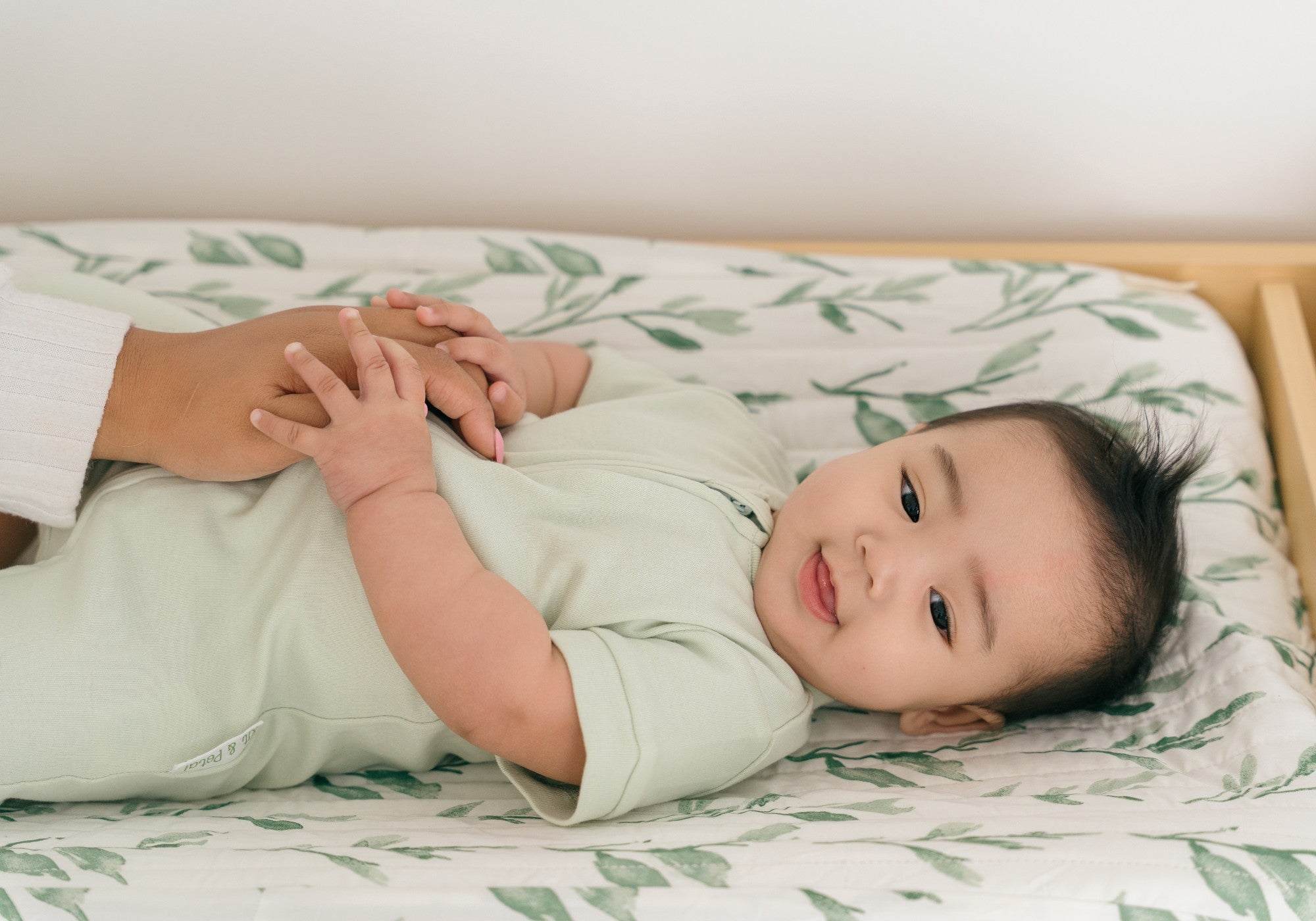 Baby wearing a leafy green short sleeve romper, laying on a changing table with a leaf print