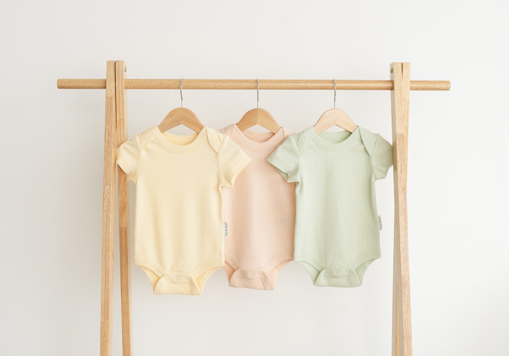 Clothing rack with three short sleeve Kit & Petal bodysuits in yellow, peach and green