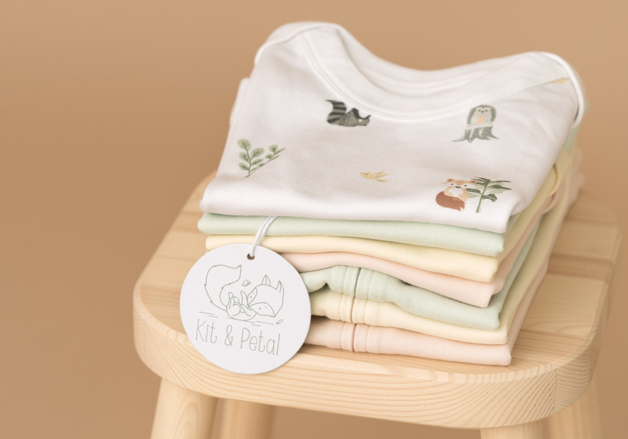 Stack of folded Kit & Petal clothing on a wooden stool,with a hangtag of Kit & Petal displayed
