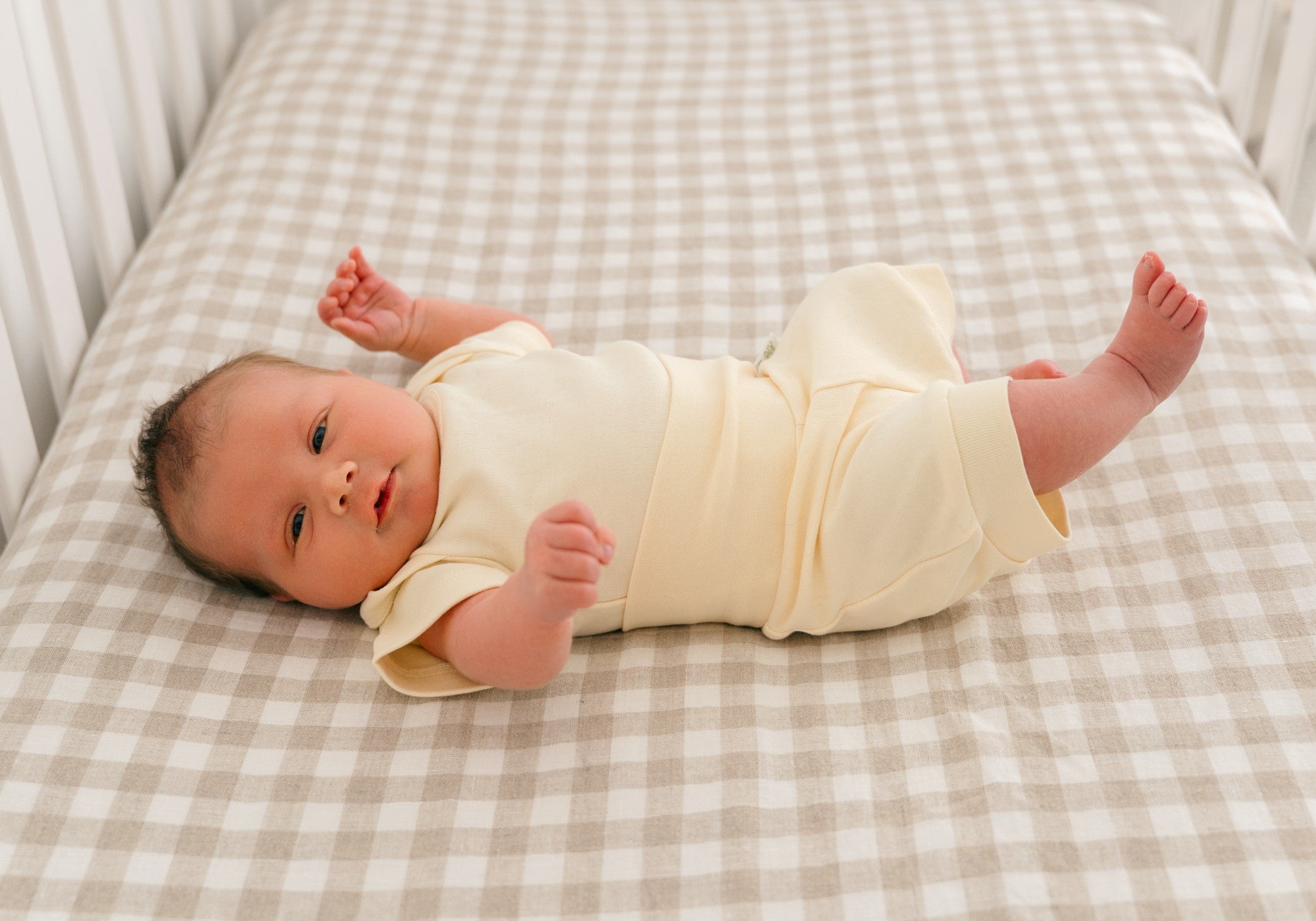 Baby laying in crib wearing Kit & Petal short sleeve bodysuit and fold-over shorts in sunny yellow