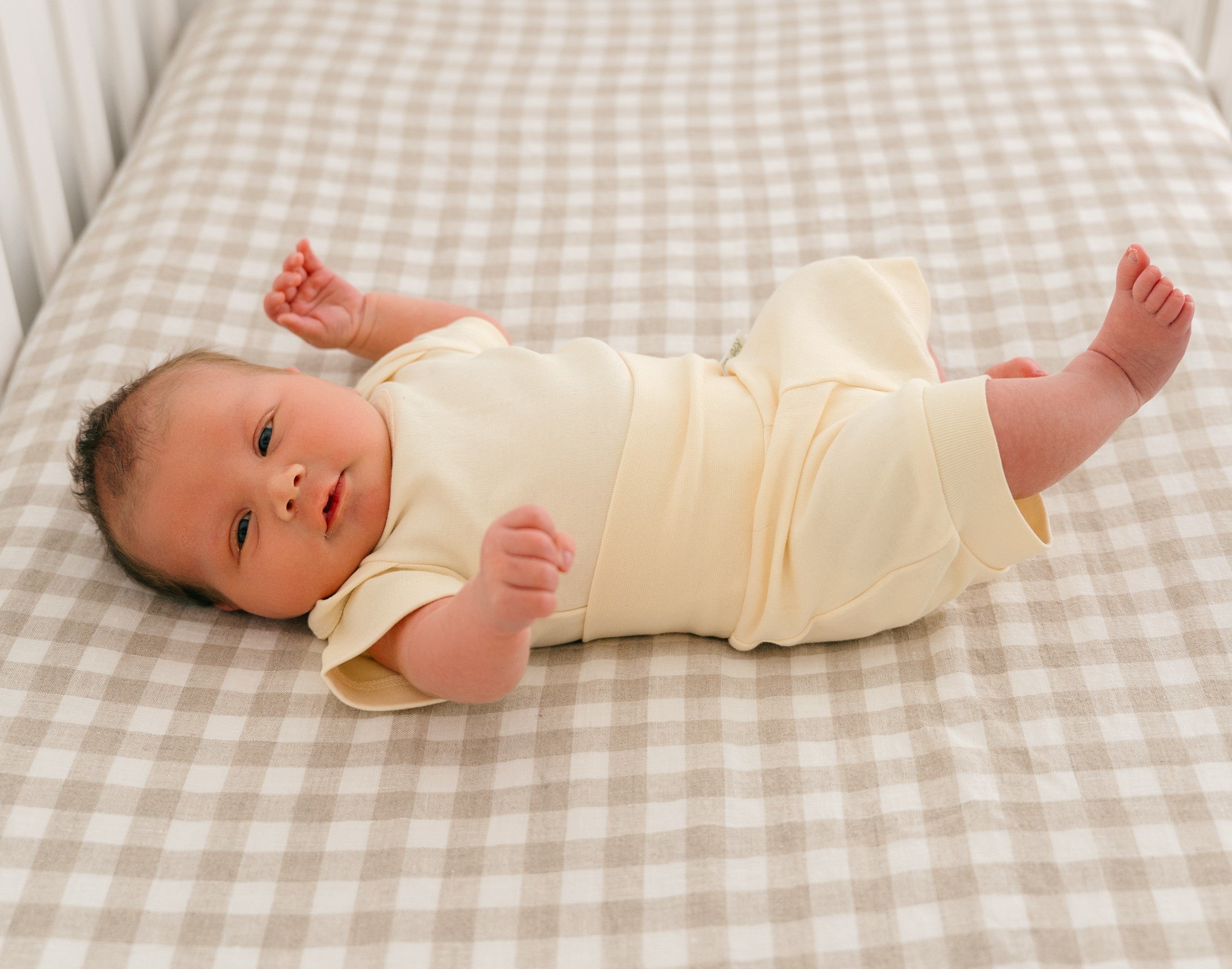 Baby laying in a crib wearing a Sunny Yellow organic cotton short sleeve bodysuit and fold-over shorts.